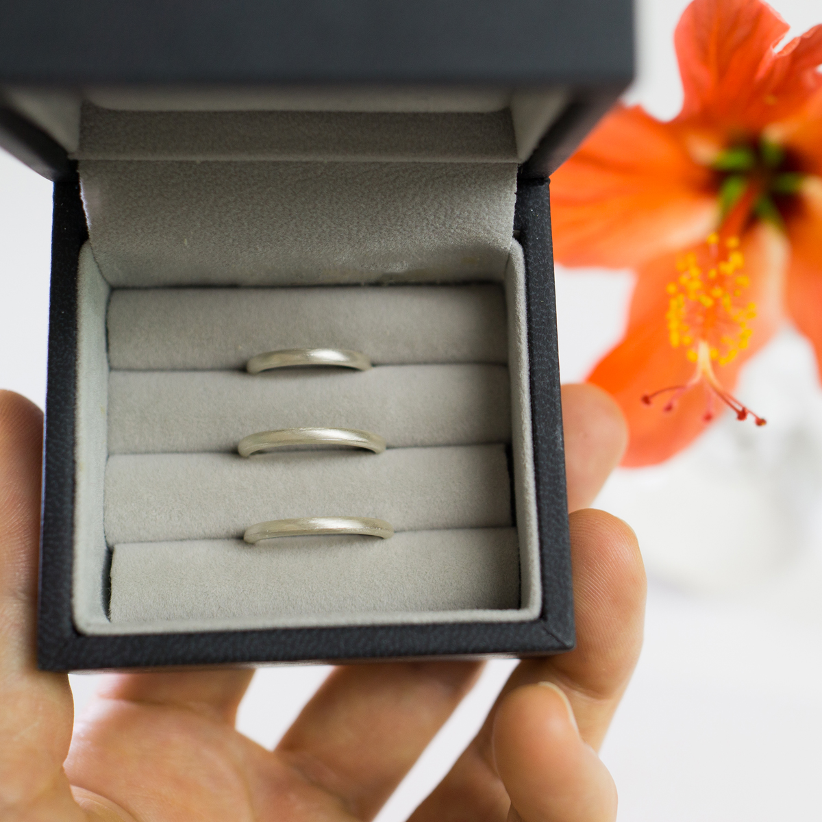 ケースの中にシルバーリング　手に持って　奥に屋久島のハイビスカス　結婚指輪のサンプル　屋久島でつくる結婚指輪